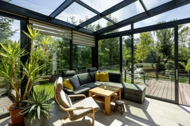 Moderní zimní zahrada s pohovkou, rostlinami a výhledem na zahradu.