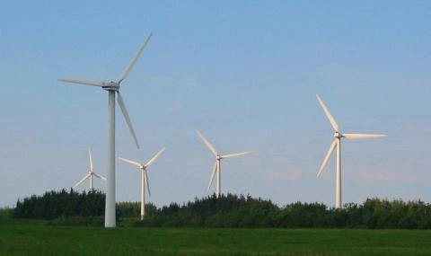 Větrné elektrárny stojí na zeleném poli pod modrou oblohou.