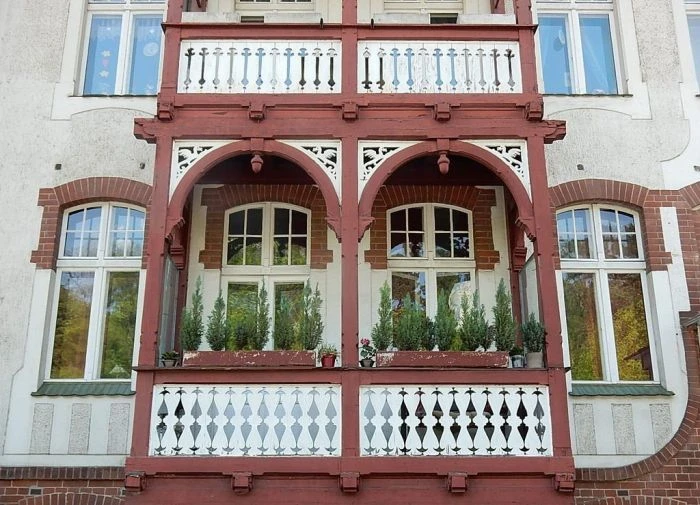Detailní fotografie červeného dřevěného balkonu s dekorativními prvky.
