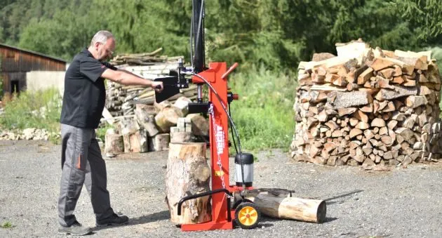 Muž rozděluje dřevo na topivo pomocí hydraulického štěpače.