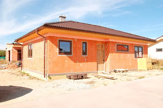 Dům z oranžových cihlových bloků při dokončování fasády.