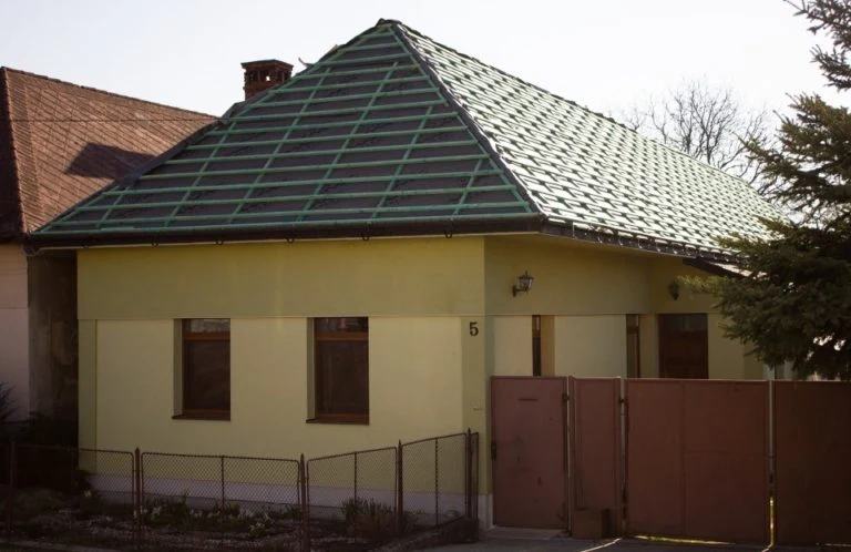 Zelená vazníková střecha s viditelnými střešními vazni na žlutém domě.