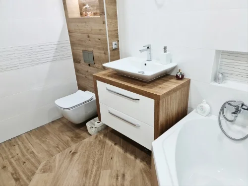 Bílá koupelna s dřevěným nábytkem a bílými sanitárními předměty.