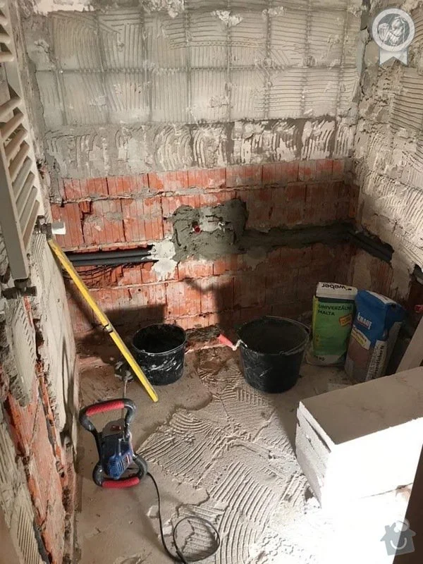 Koupelna v rekonstrukci s omítkou na podlaze a cihlovými zdmi.