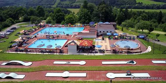 Vzdušný pohled na venkovní bazénový komplex s vodními skluzavkami a okolním krajinným pozadím.