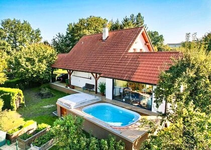Dům s bazénem v zahradě na pozadí zelených stromů.