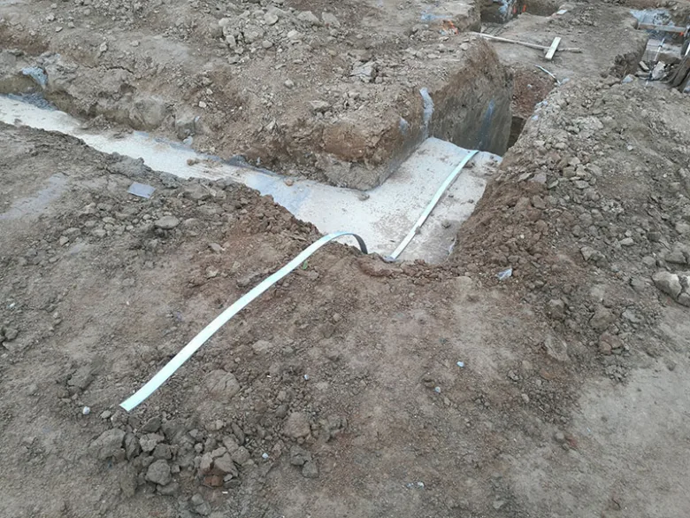 Bílý vodič uzemnění položený v příkopu pro elektroinstalaci.