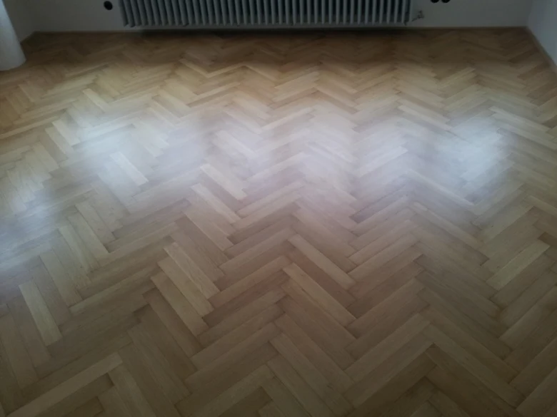 Lesklá parketová podlaha v šachovnicovém vzoru po renovaci.