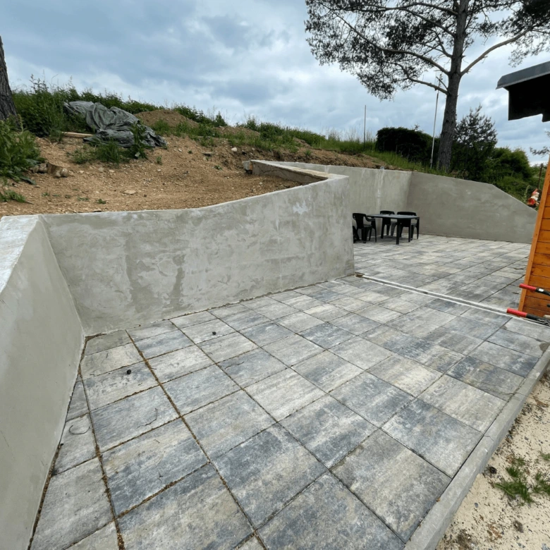 Nová betonová terasa s kamennou dlažbou a zádržnými zdmi.