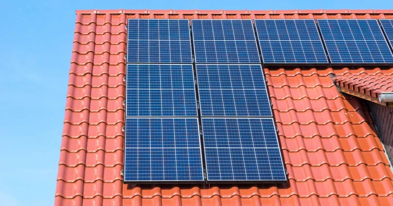 Modré fotovoltaické panely na červené střechě domu.