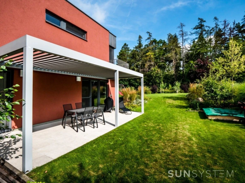 Bioklimatická pergola s venkovním nábytkem u domu v zahradě.
