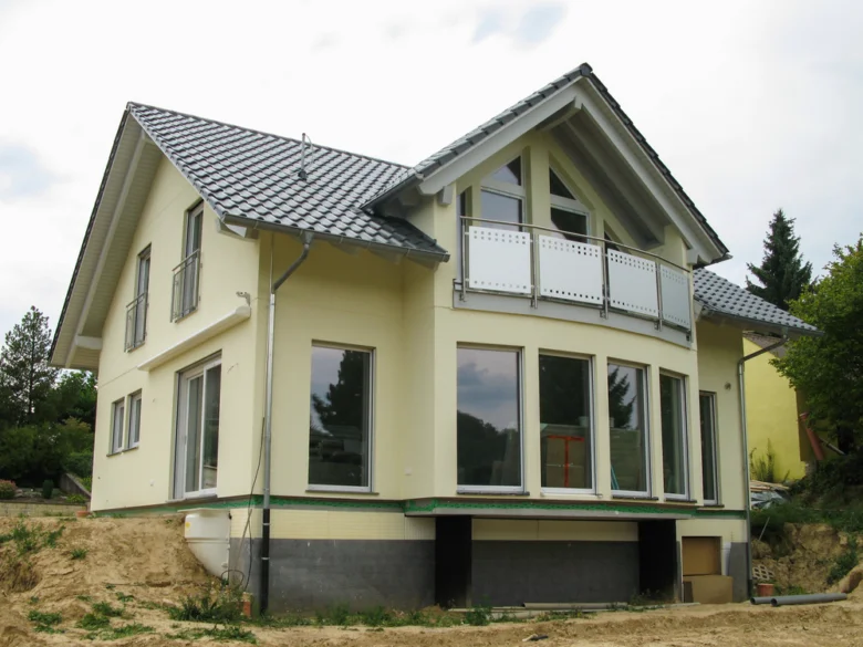 Dvoupatrový dům s fasádou v krémové barvě na nezpevněném pozemku.