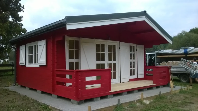 Červená dřevěná přístavba s terasou postavená na pozemku.