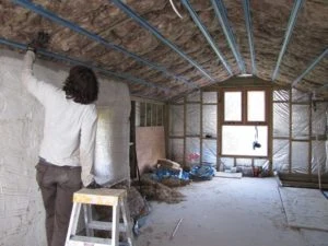 Muž instaluje tepelnou izolaci do krovu v nehotové střeše.