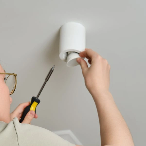 Osoba montuje stropní svítidlo s šroubovákem a ručně upravuje elektrický komponent.
