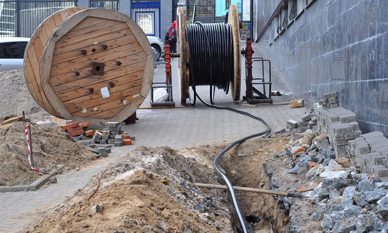 Výkop pro uložení elektrického kabelu s bubnem na pozadí.