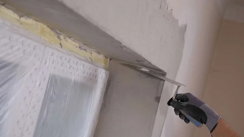 Ruční aplikace špachtlí na stěnu u okenního rámu.
