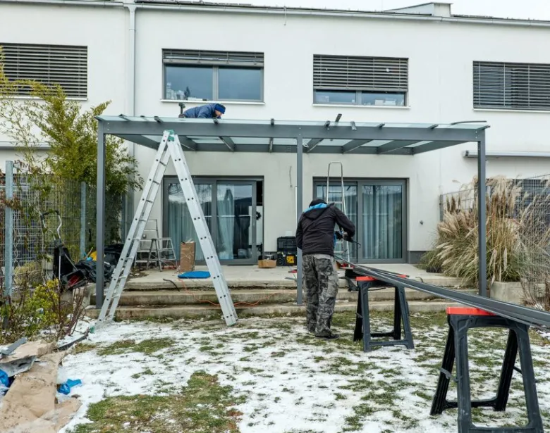 Stavba kovové pergoly u domu s dělníky na zahradě.