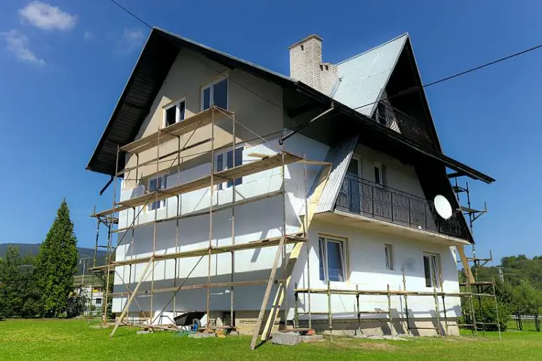 Dřevěný dům s oporou pro zateplení fasády na slunci.