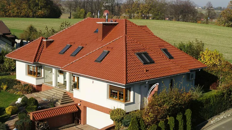 Rodinný dům s červenou sedlovou střechou na pozadí zelených polí.