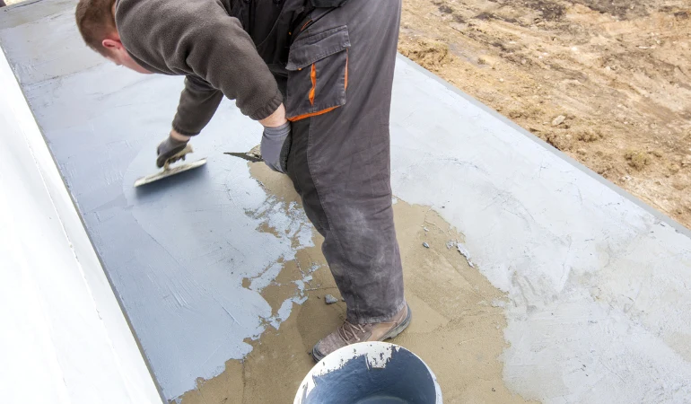 Stavebník hladí čerstvý beton pro terasu u domu.