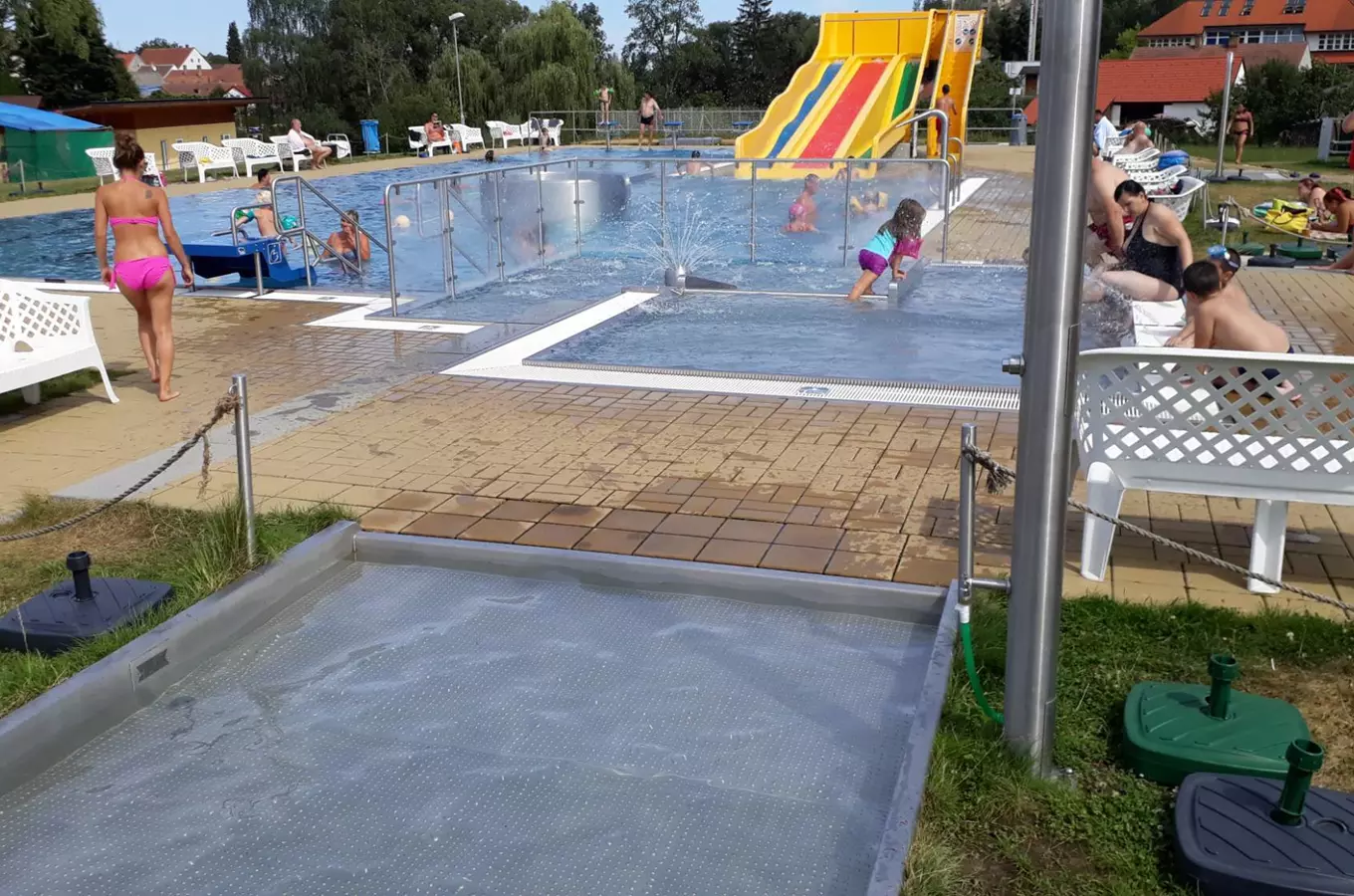 Venkovní bazén ve Velešíně s dětským skluzavkou a lidmi v koupališti.