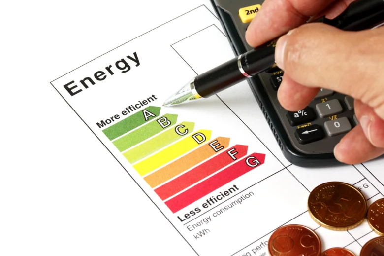 Ruka s tužkou nad tabulkou energetické účinnosti vedle kalkulačky.