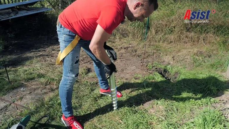 Muž ručně vrtá do země pro dřevní přístřešek.