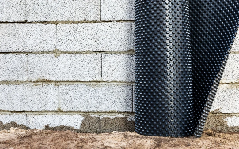 Černá drenážní desita je montována na betonový základ stěny.
