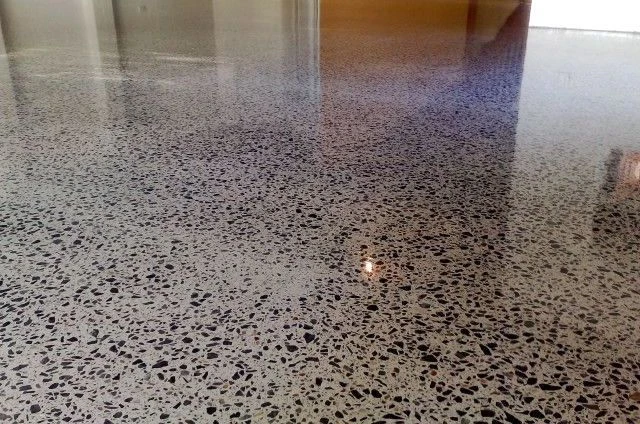Lesklá betonová podlaha s vloženými kameny v interiéru.