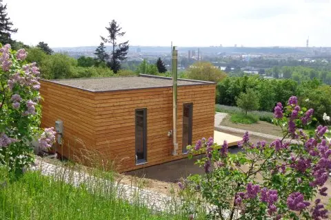 Modulový dřevěný dům pro celoroční bydlení na svahu s kvetoucími lilijemi.