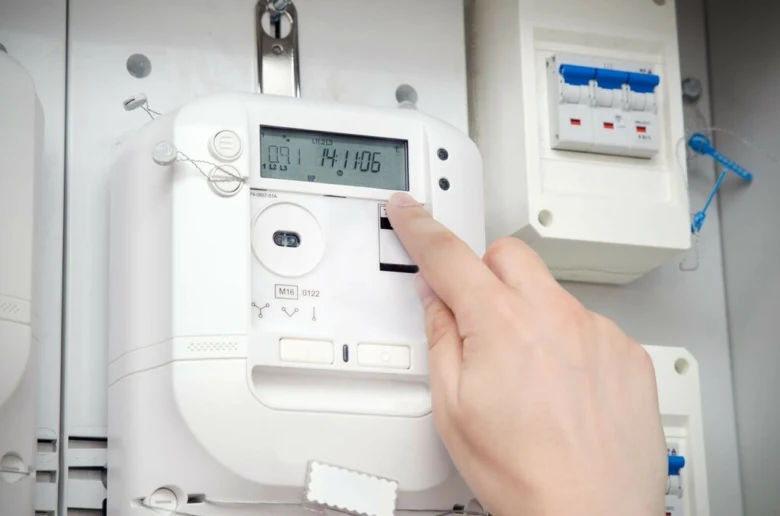 Ruka stiská tlačítko na elektroměru pro odečtení čísel.