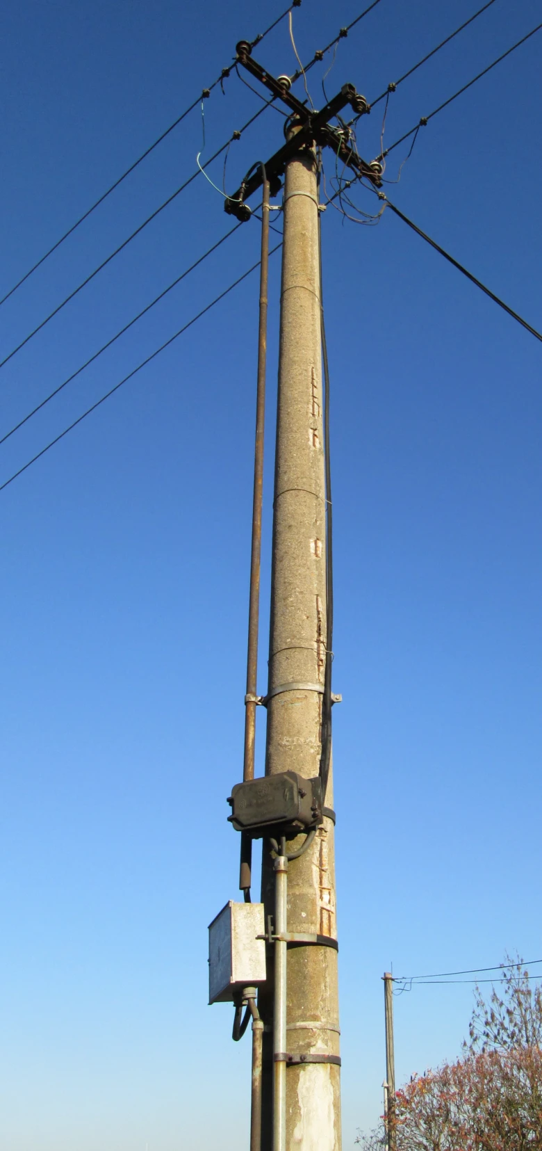 Konkrétní betonový sloup s elektrickými vedením na modré obloze.