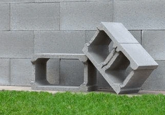Dva betonové prázdné bloky na trávníku před zdí.