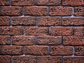 Detailní záběr na červenohnědou texturovanou cihlovou fasádu pro obklad.