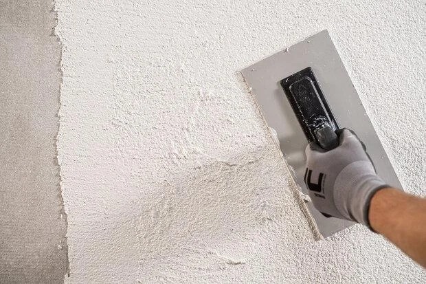 Ruční aplikace minerální omítky na stěnu pomocí špachtle.
