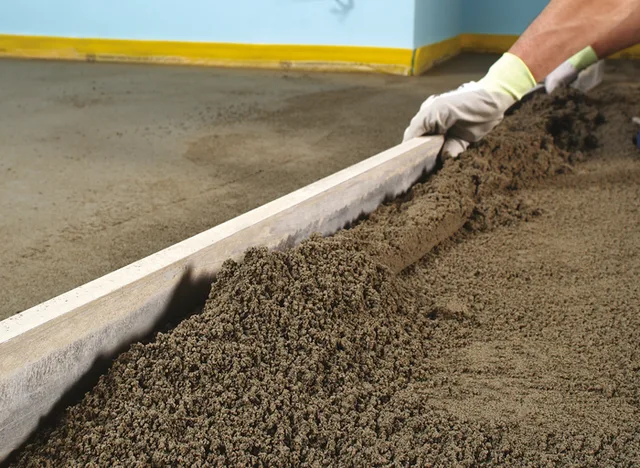 Pracovník vyrovnává čerstvý beton na podlahu pomocí pravítka.