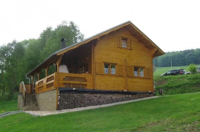 Dvoupatrová dřevěná chata na kamenném základe v zelené krajině.