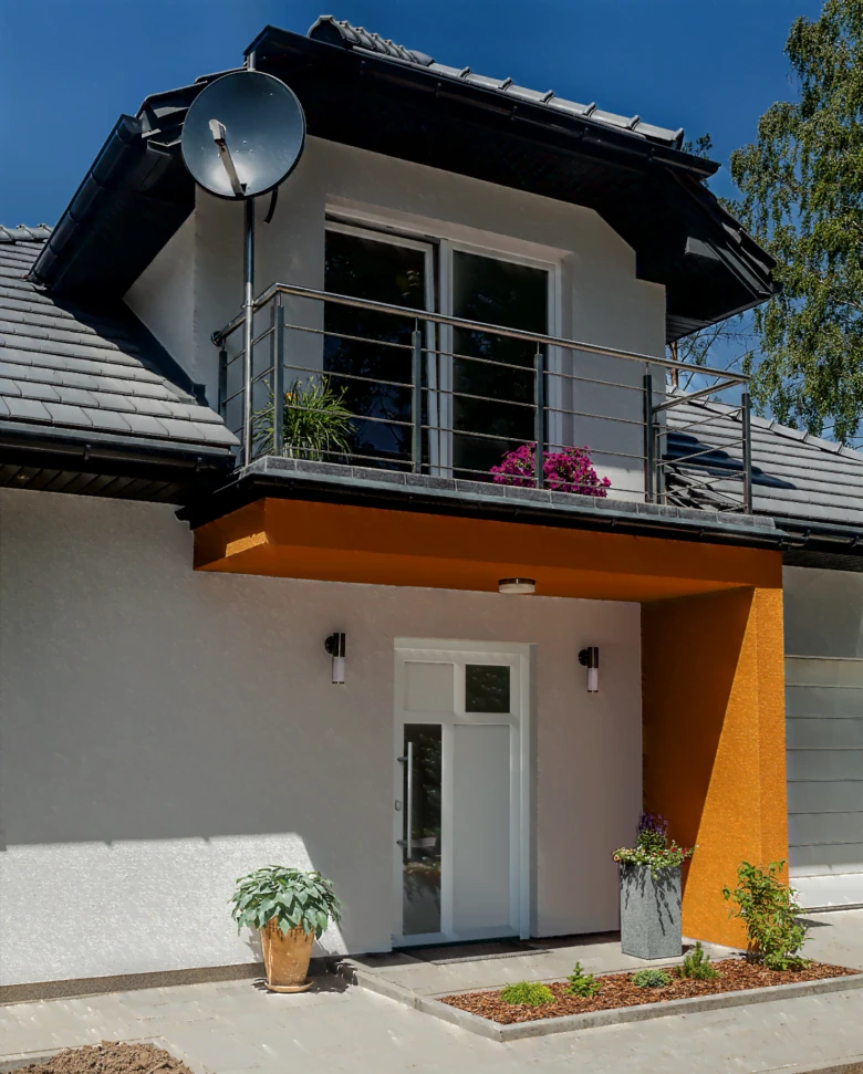 Moderní venkovní dveře s oranžovým přístavkem na fasádě domu.