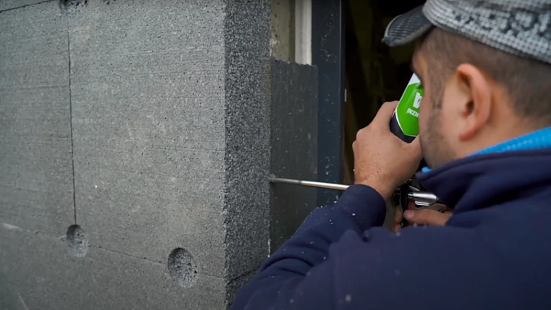 Pracovník izoluje ostění okna pomocí pěnového těsnicího materiálu.