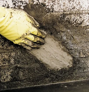 Ruční aplikace hydroizolačního stěrku na zdivo pro vytvoření vodotěsné vrstvy.