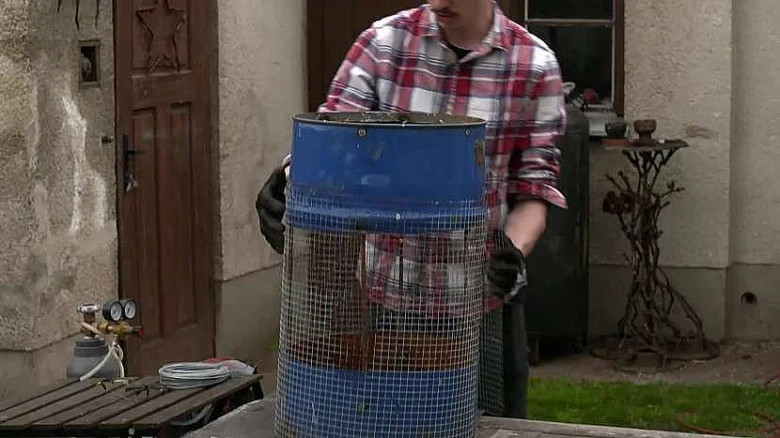 Muž drží modrou barel síto na prosévání zeminy pro zahradu.