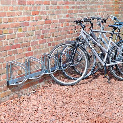 Kovový stojan na kola u zdi s několika bicykly.