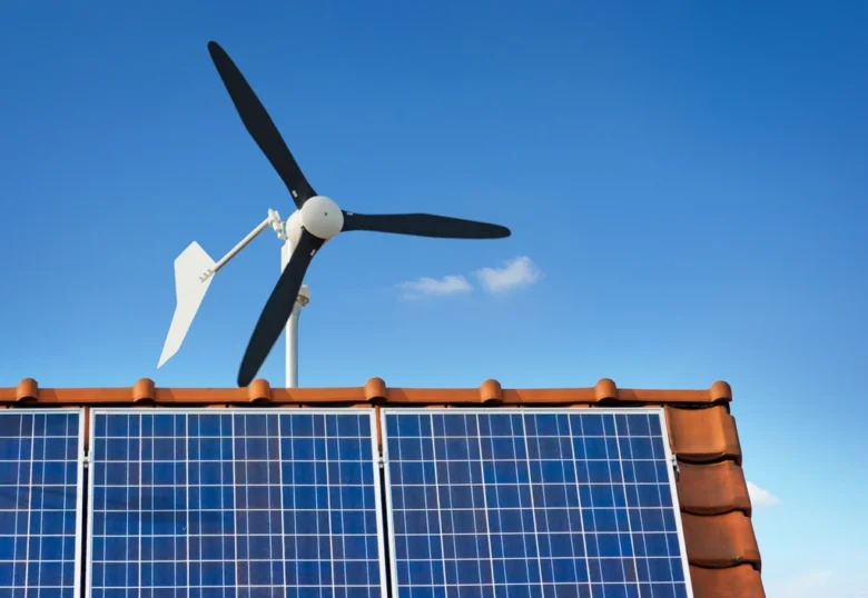 Malá domácí větrná turbína na střechě s fotovoltaickými panely.