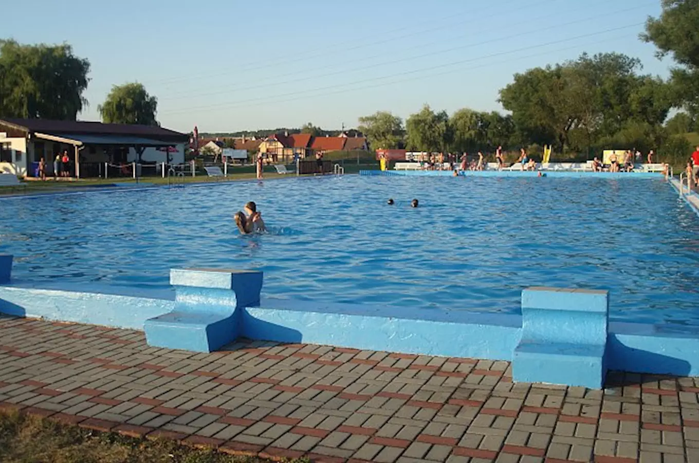Venkovní bazén v Olesniku s lidmi ve vodě a na okraji.