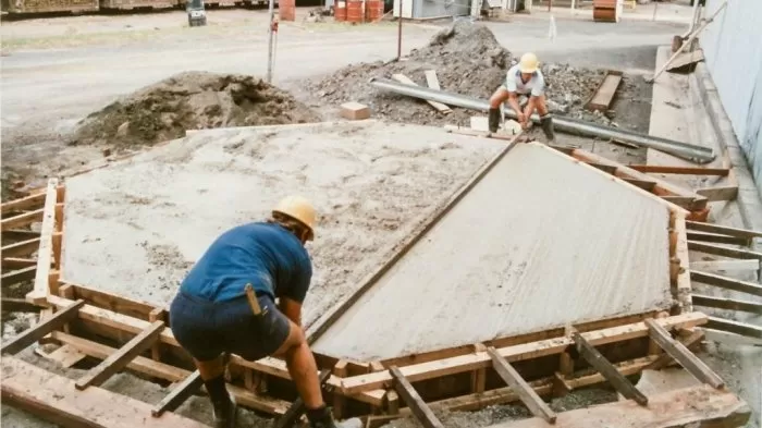 Dva dělníci nalévají beton do dřevěného patka pro dřevostavbu.