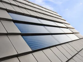 Fotovoltaické tašky integrované do střechy domu pod modrou oblohou.