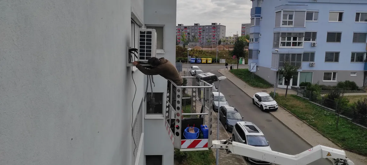 Technik čistí klimatizační jednotku na fasádě budovy v Brně.