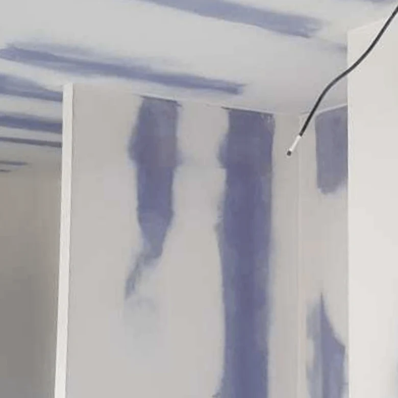 Náplňování spár sádrokartonu modrou hmotou na stěně.