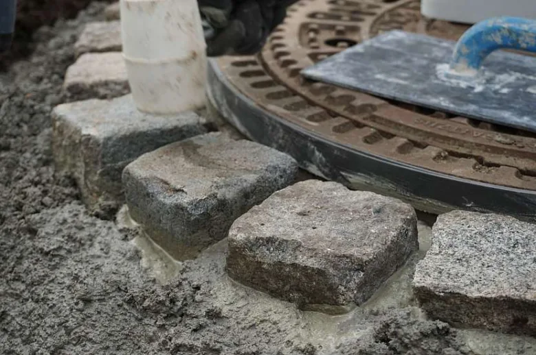 Kamenná dlažba se zasazuje do čerstvého betonu u potrubí.